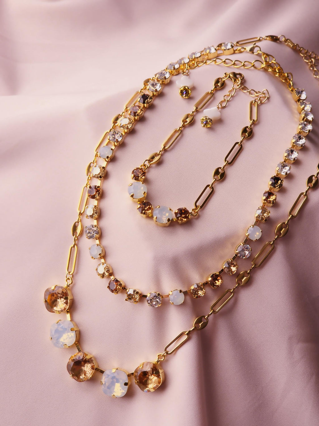 A gold-toned layered necklace set with mixed gemstone beads, displayed on a soft pink satin fabric background.