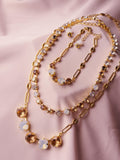 A gold-toned layered necklace set with mixed gemstone beads, displayed on a soft pink satin fabric background.
