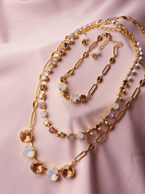 A gold-toned layered necklace set with mixed gemstone beads, displayed on a soft pink satin fabric background.